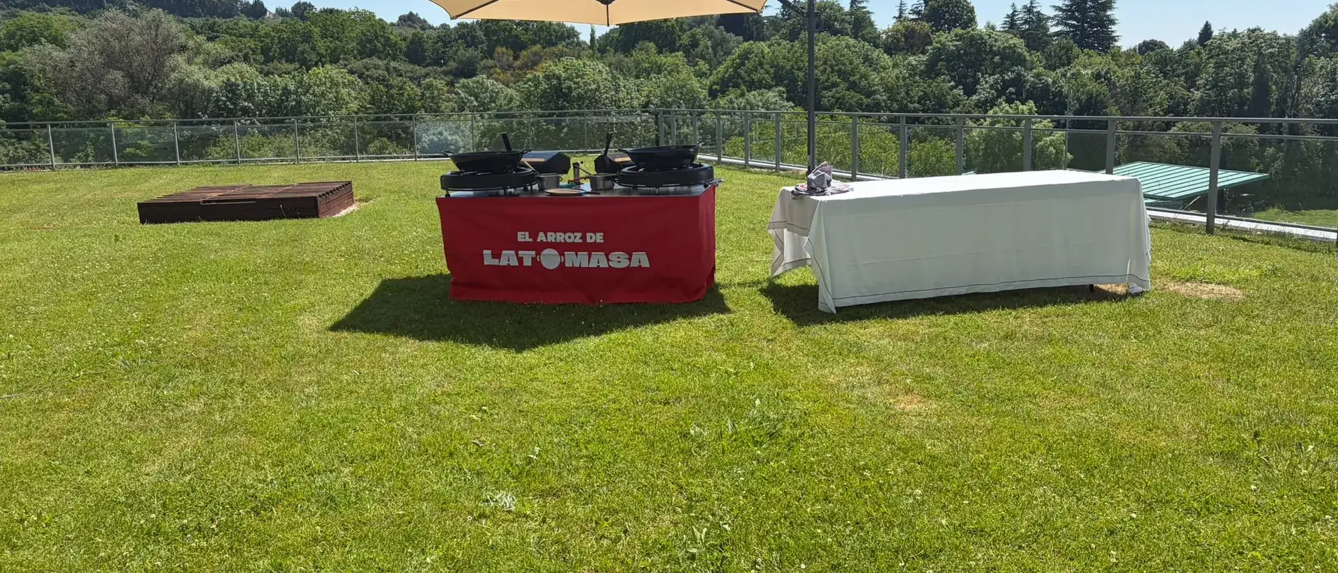 Montaje del servicio de paella sobre el césped de una finca, con sombrilla y mesa de servicio