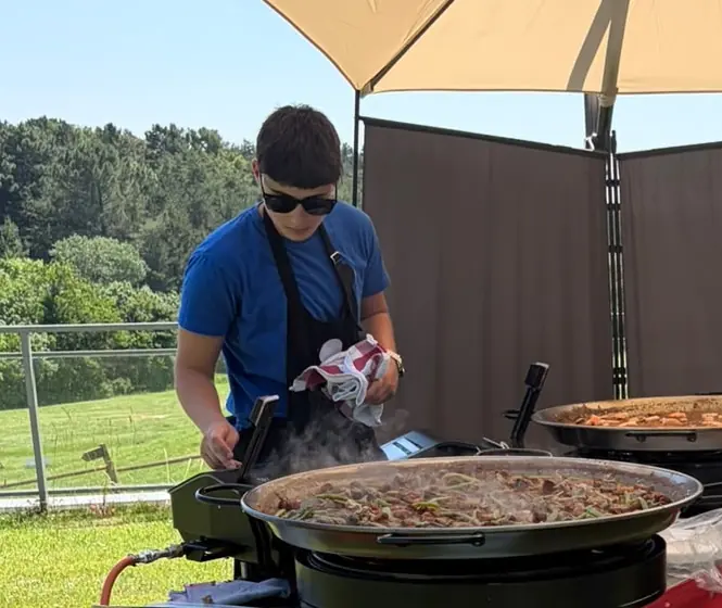 Cocinera de El Arroz de LaTomasa preparando una paella en el paellero durante un evento