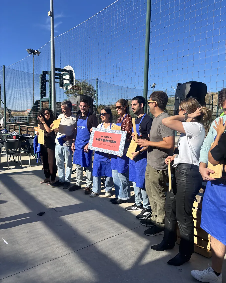 Grupo de una empresa con delantales y el cartel de El Arroz de LaTomasa tras un taller de paella
